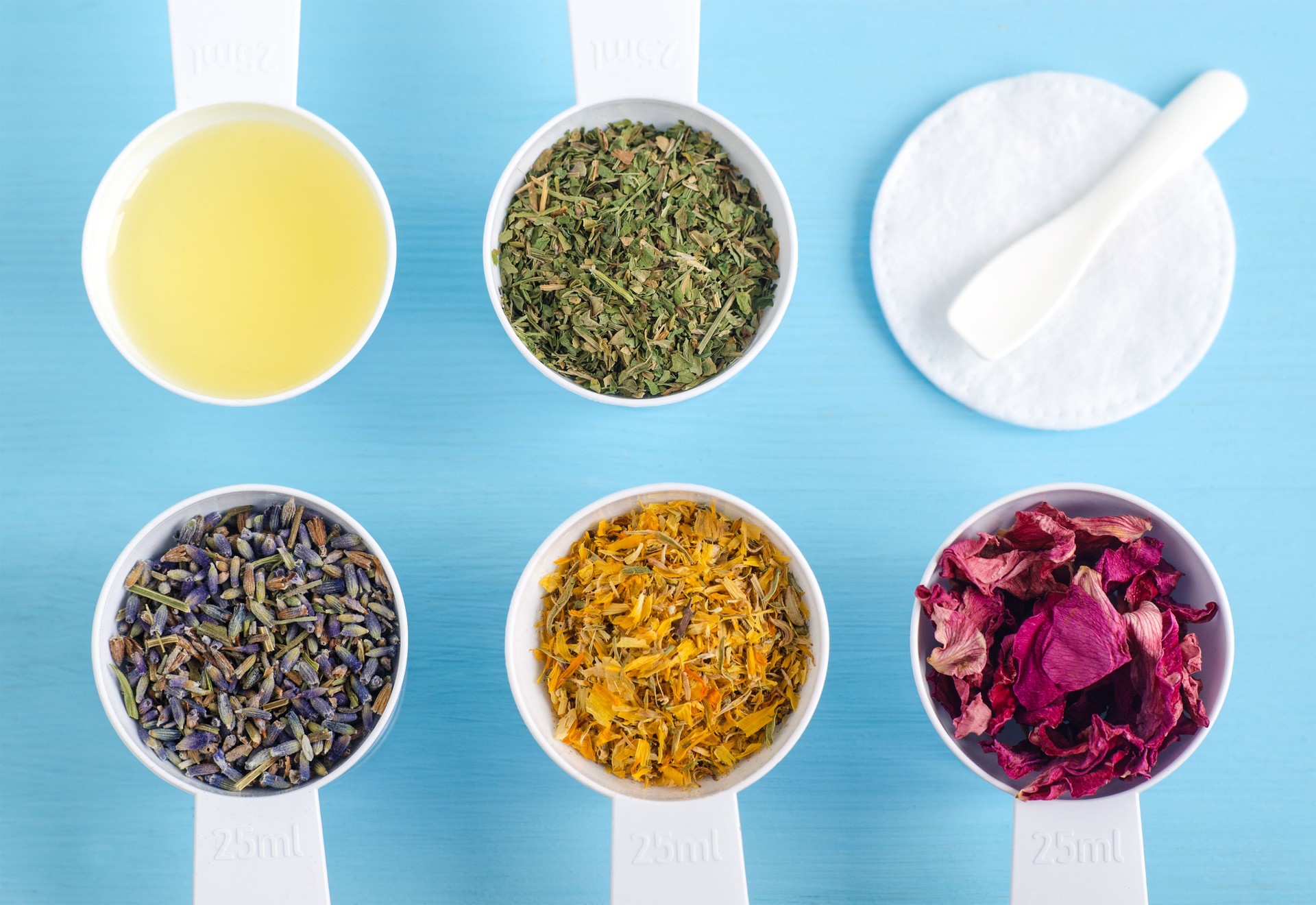 Plastic scoops with olive oil and various healing herbs - dry parsley, marigold, lavender and dog rose flowers. Aromatherapy, herbal medicine and natural skin care concept. Top view, copy space.